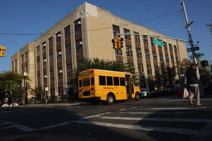 Exterior of PS 166 in Queens, seeing the four story building from across the street with a school bus passing by